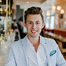 Smiling young man in white shirt with teal pocket square in a café setting.