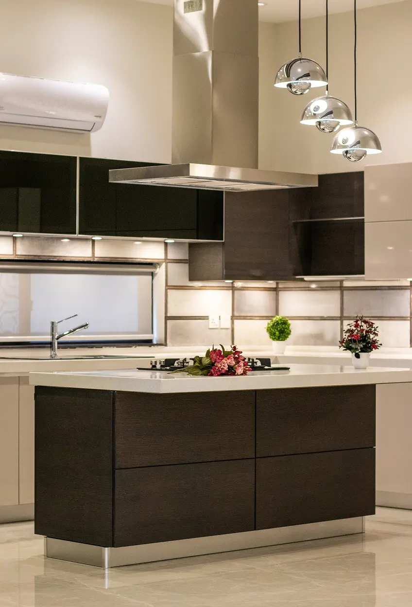 Modern kitchen with dark island, white countertop, built-in stove, hanging pendant lights, and decorative plants.